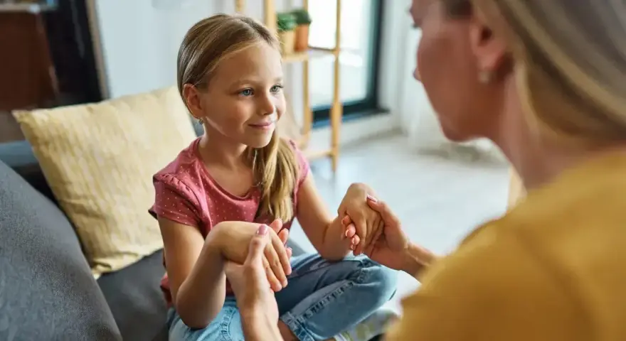 Mama spokojnie tłumaczy córce, jak rozmawiać z dzieckiem o złym zachowaniu. Dziecko słucha uważnie, trzymając dłonie mamy.