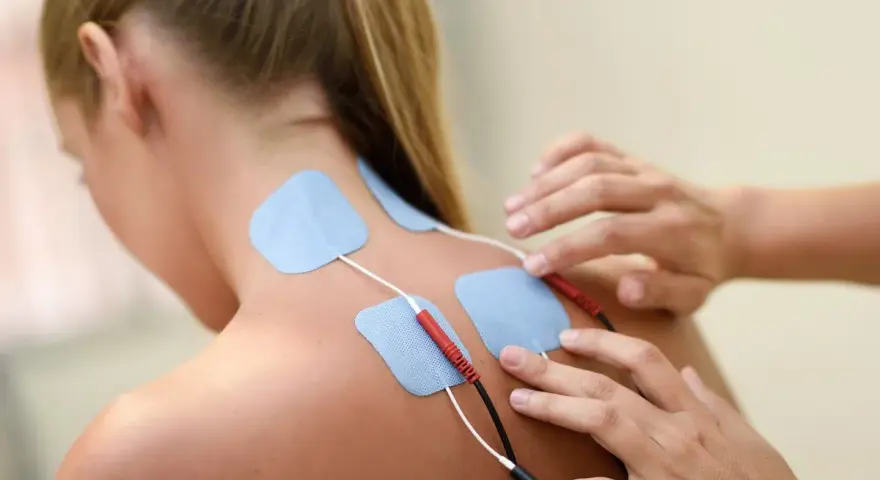 Elektrody na plecach kobiety podczas terapii fizykalnej. Terapeuta przygotowuje do zabiegu.