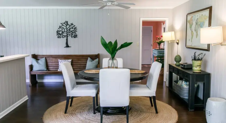 Elegante decoracion comedor pequeño con mesa redonda, sillas blancas, banco de madera y arte de árbol en la pared.