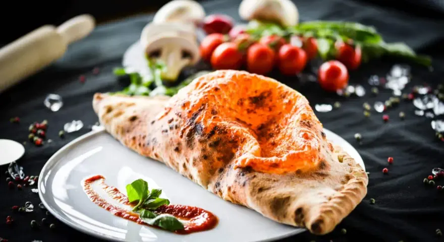 Ein köstlicher, original italienischer Calzone, goldbraun gebacken, mit Tomatensoße und Basilikum garniert.