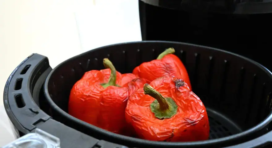 Tre peperoni rossi interi, leggermente abbrustoliti, pronti per essere cucinati nella friggitrice ad aria.