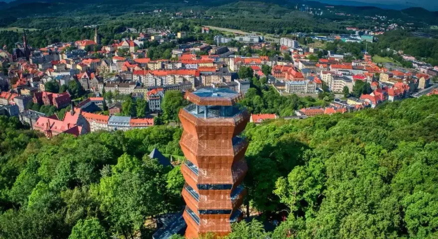 Nowoczesna wieża widokowa w otoczeniu zieleni, z panoramą miasta Wałbrzych i Sudetów Wałbrzyskich w tle.