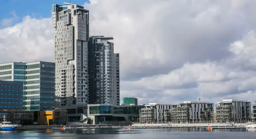 Nowoczesne budynki w Gdyni, w tym wysoki Sea Tower, nad wodą przy pochmurnym niebie.