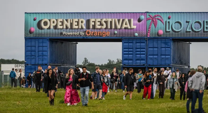Tłum ludzi wchodzi na teren festiwalu. Nad nimi brama z napisem "OPEN'ER FESTIVAL". Kto będzie następny?