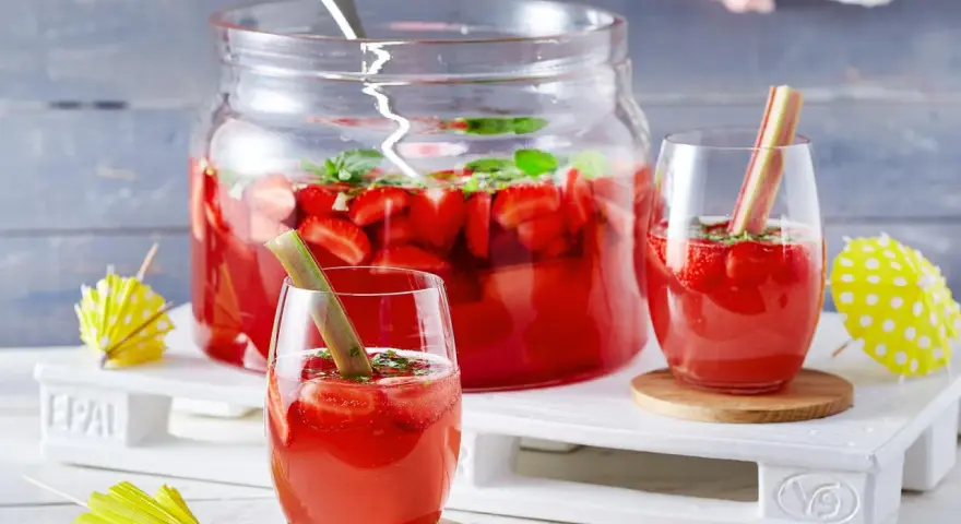Erfrischende Rhabarber Bowle mit Erdbeeren und Minze, garniert mit Rhabarberstücken. Perfekt für den Sommer!
