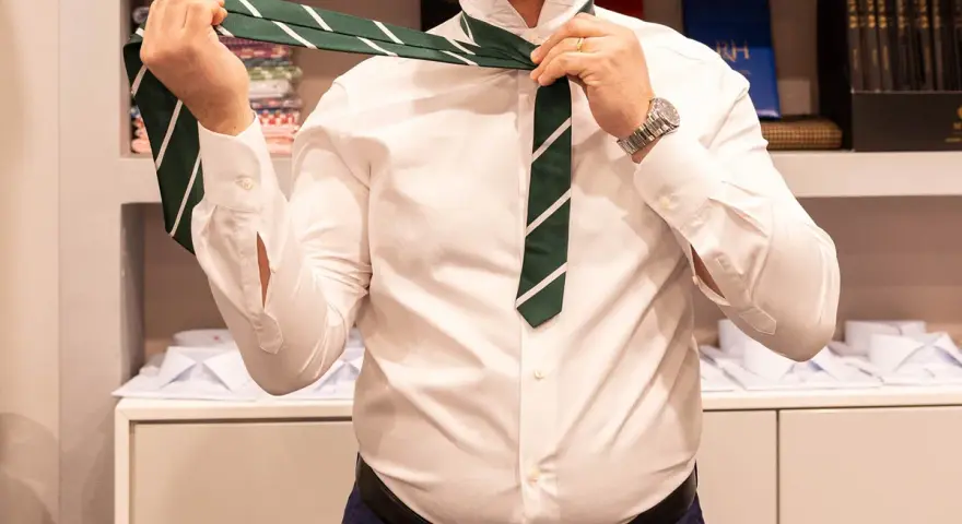 Uomo in camicia bianca che impara come fare il nodo alla cravatta verde a righe.