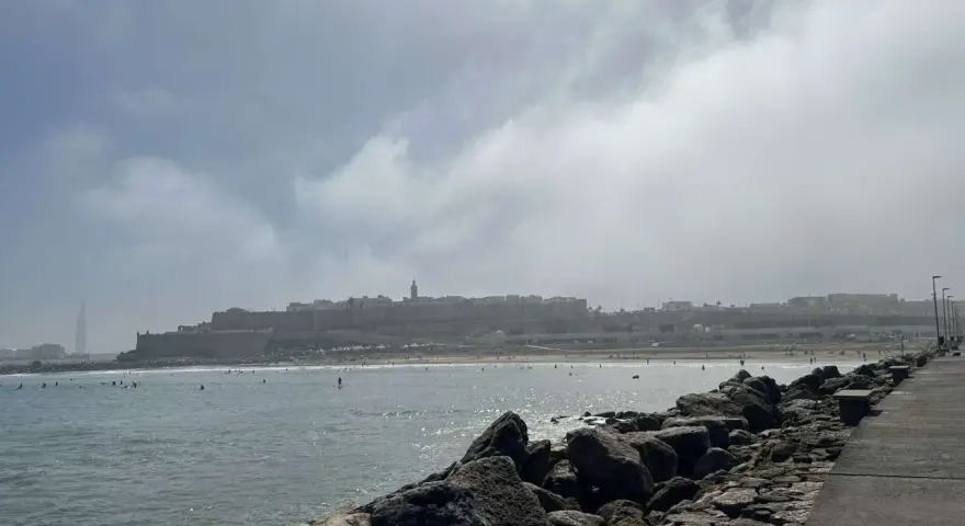 Spokojna plaża z surferami i miastem w tle. Czy Maroko jest bezpiecznym krajem? Widok sugeruje, że tak, ludzie cieszą się słońcem i morzem.
