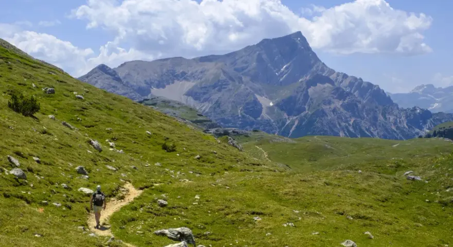 Escursionista su sentiero erboso, con imponente gruppo montuoso delle Dolomiti sullo sfondo.
