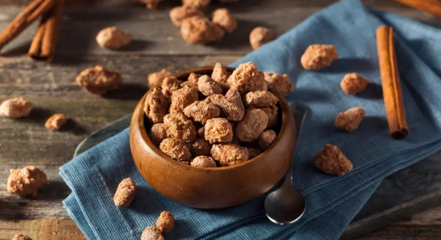 Schüssel mit gebrannten Mandeln, Zimtstangen und Löffel. Ein süßer Snack, der auch in der Schwangerschaft genossen werden kann.