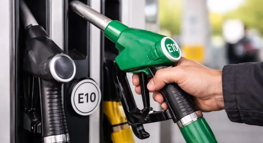 Mano che impugna una pompa di benzina verde con etichetta E10, pronta per fare rifornimento di benzina 95 ottani.