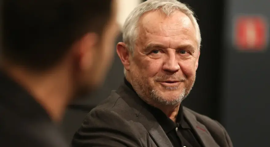 Uśmiechnięty Mikołaj Kondrat w szarym garniturze, rozmawiający z kimś niewidocznym na pierwszym planie.