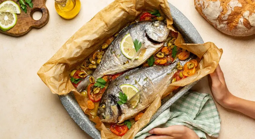 Due agoni in carpione cotti al forno con pomodorini, olive e limone, pronti per essere gustati.