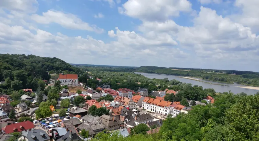 Widok na Kazimierz Dolny z górami Trzech Krzyży w tle. Rzeka Wisła, zielone wzgórza i urokliwe miasteczko z czerwonymi dachami.