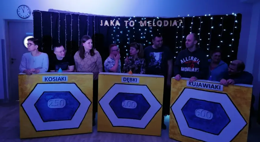 Uczestnicy zabawy "Jaka to melodia?" stoją przy planszach z nazwami drużyn: Kosiaki, Dębki, Kujawiaki.