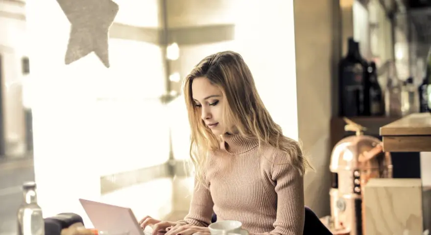 Kvinna skriver tack mail efter intervju på sin laptop vid ett bord med en tekanna.