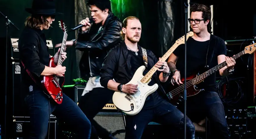 Zespół gra na scenie, wokalista śpiewa, gitarzyści i basista tworzą muzykę. Może to piosenka "Kocham Cię".