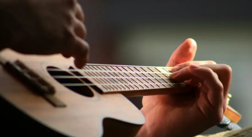 Dłonie grające na ukulele, zbliżenie na gryf i struny.