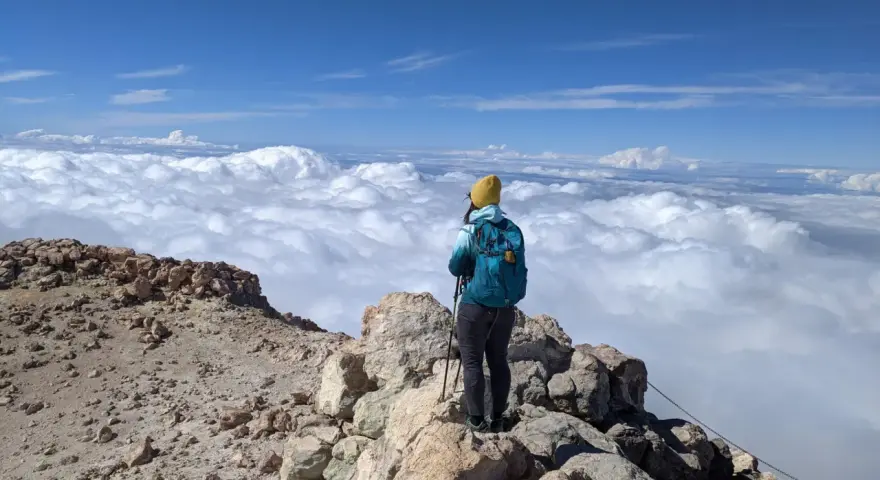 Widok z Teide: turystka w żółtej czapce podziwia morze chmur z wulkanicznego szczytu.