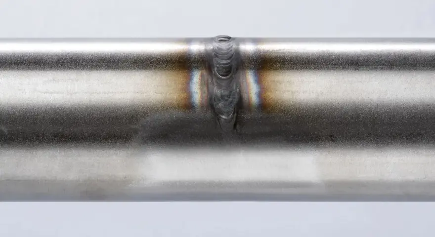 Dettaglio di una saldatura acciaio inox su un tubo metallico, con sfumature iridescenti intorno al cordone.