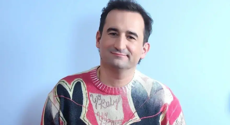 Uśmiechnięty polski aktor z autyzmem w kolorowym swetrze z sercem i napisem "Yo Baby".