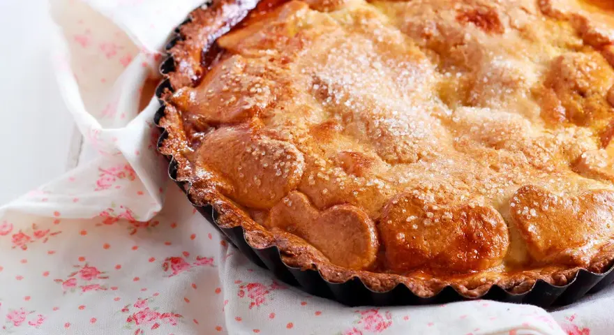 Une délicieuse tarte au sucre dorée, saupoudrée de cristaux de sucre, repose sur une serviette à motifs floraux roses.