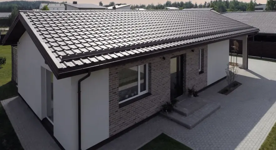 Nowoczesny dom z ceglaną elewacją i białymi tynkami, przykryty ciemnym dachem jednospadowym. Podjazd z kostki brukowej.