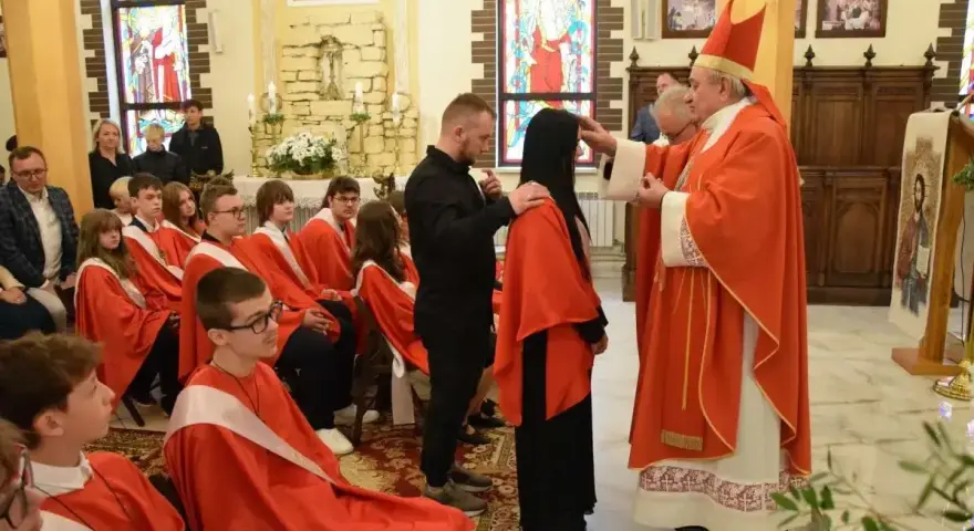 Biskup udziela sakramentu bierzmowania. Ceremonia, choć uroczysta, nie trwa długo. Młodzi ludzie w czerwonych szatach czekają na swoją kolej.