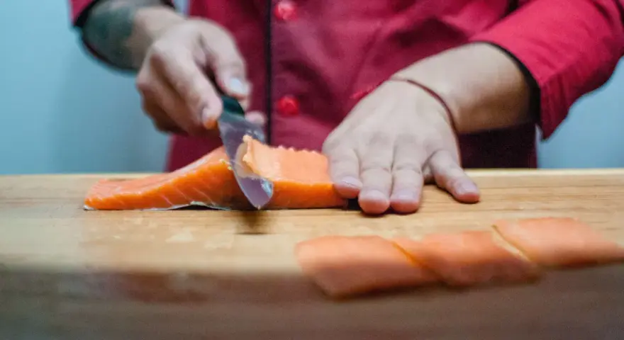 Szef kuchni kroi łososia na desce. Powstają kawałki idealne do sushi, które można zamarynować w solance.