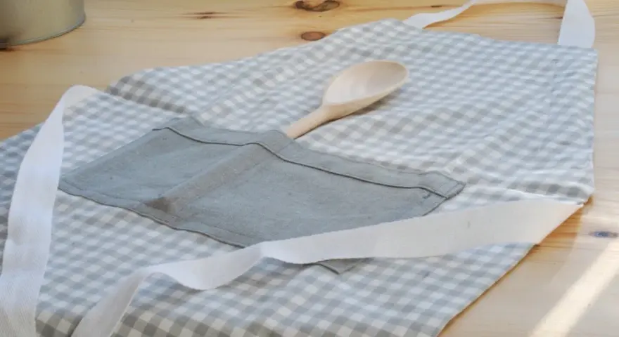 Gotowy fartuch kuchenny w kratkę, z drewnianą łyżką w kieszeni. Idealny poradnik, jak uszyć fartuch kuchenny.