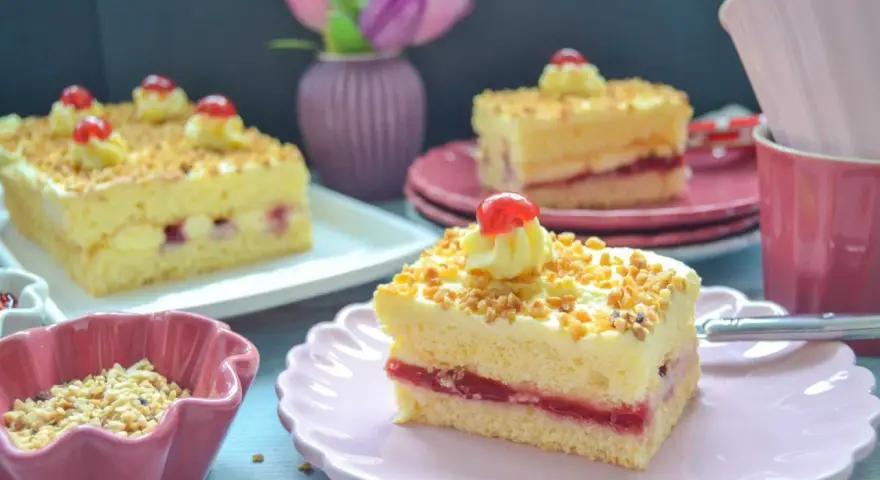 Stückchen eines Frankfurter Kranz Blechs mit Buttercreme, Kirschen und gehackten Nüssen.