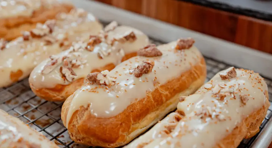 Éclairs dorés sur une grille, nappés d'un glacage sirop d'érable et parsemés de noix concassées. Un délice gourmand.