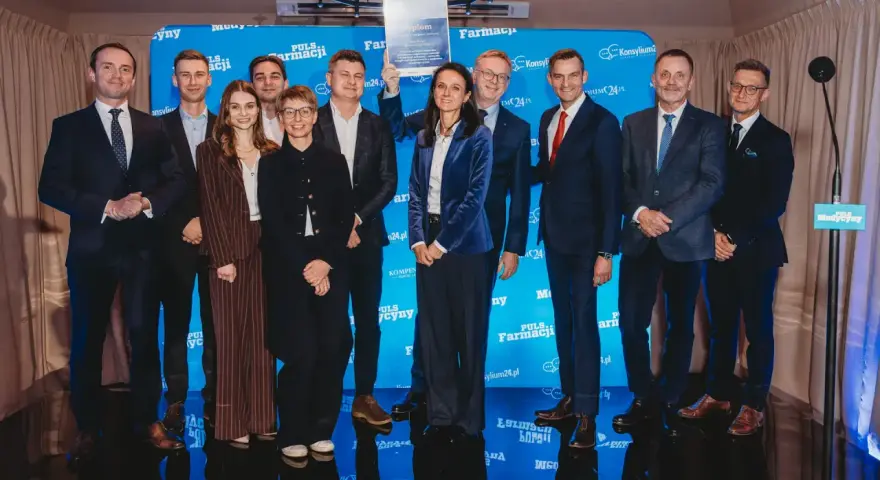 Grupa ludzi na scenie, wśród nich Janusz Sowa, odbiera dyplom. W tle niebieskie banery z logo Puls Farmacji.