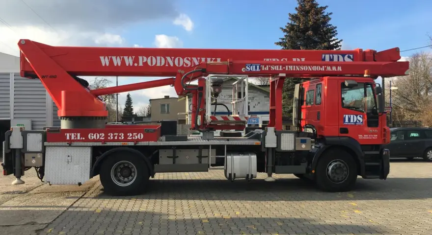Czerwony podnośnik koszowy WUMAG WT 450 z koszem roboczym i wysięgnikiem. Na pojeździe widnieje napis WWW.PODNOSNIKI-TDS.PL.