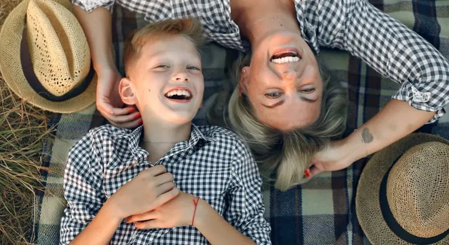 Uśmiechnięta mama i syn leżą na kocu. Idealny dzień na życzenia z okazji Dnia Mamy.