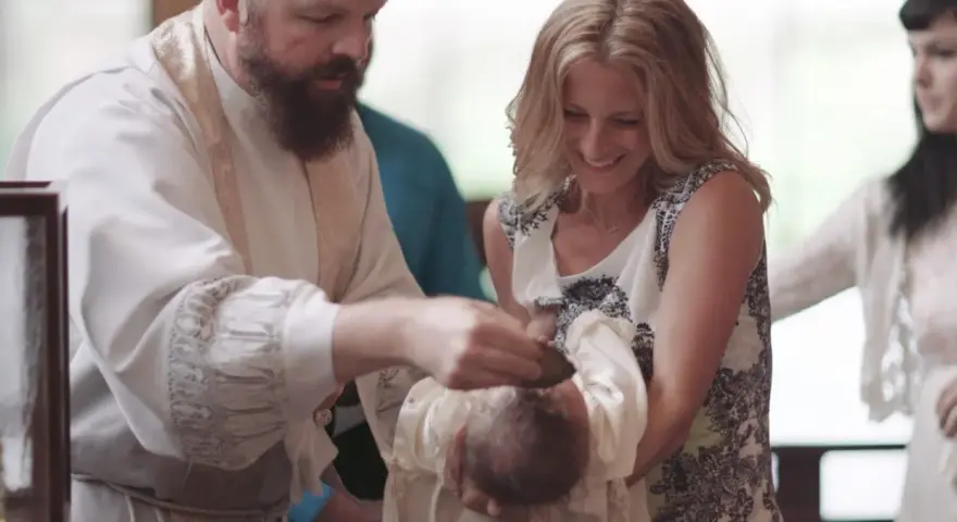 A priest performs a baptism, pouring water on a baby's head. The mother smiles, holding her child. This image captures the sacred moment of how to baptize someone.