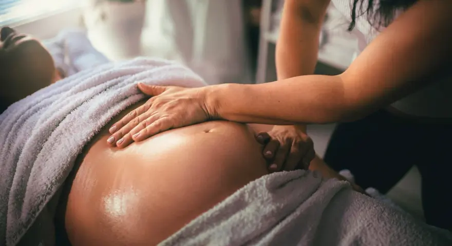 Delikatny masaż w ciąży. Dłonie terapeuty obejmują zaokrąglony brzuch przyszłej mamy, przynosząc ulgę i relaks.