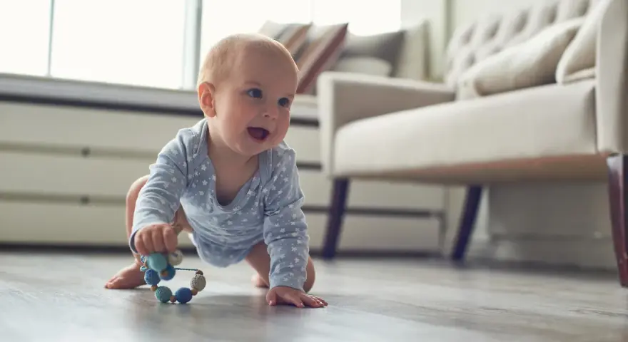 Ein Baby in blauem Sternen-Body krabbelt fröhlich über den Holzboden und greift nach einer bunten Rassel. So erkunden Babys die Welt!