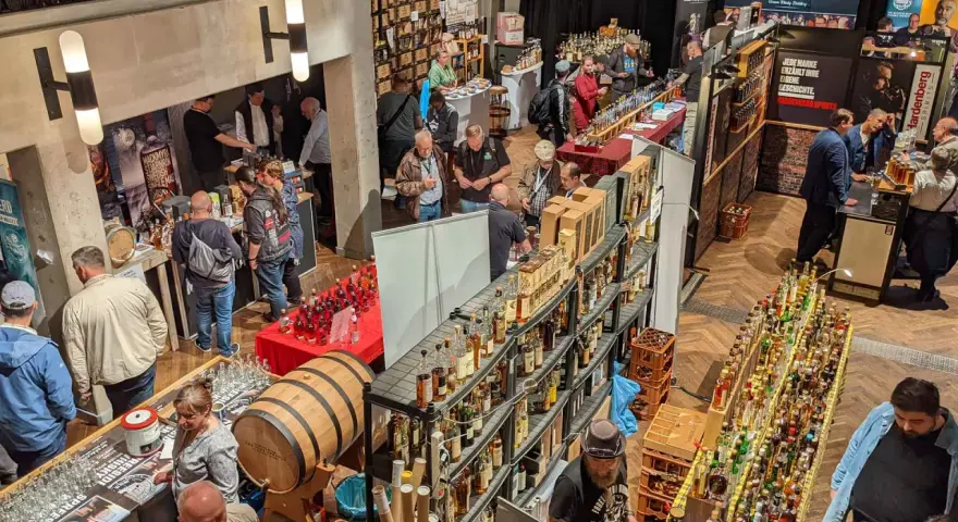 Besucher auf einer Messe probieren Spree-side Whisky. Viele Flaschen und ein Fass sind ausgestellt.