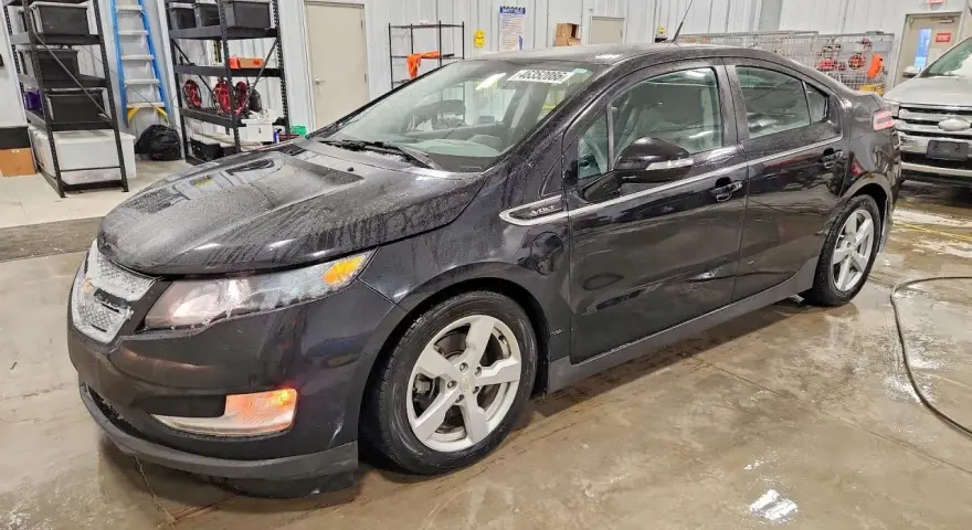 Czarny Chevrolet Volt stoi w garażu, mokry od deszczu. W tle regały z narzędziami i drabina.