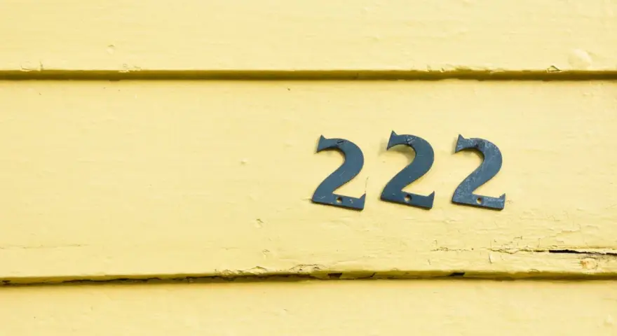 Na żółtej, drewnianej ścianie widnieje anielska liczba 222.