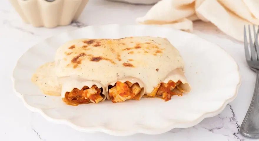 Canelones de atún gratinados con bechamel cremosa, listos para disfrutar en un plato blanco con borde ondulado.