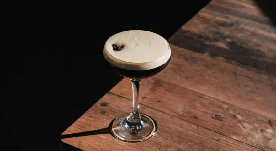 Elegancki por star martini z pianką i ziarnem kawy, stojący na drewnianym stole w cieniu.