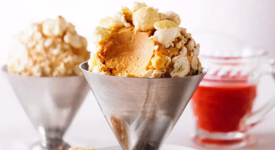 Cremiges Karamell-Popcorn-Eis in einem Metallbecher, garniert mit knusprigem Popcorn. Ein süßer Genuss!