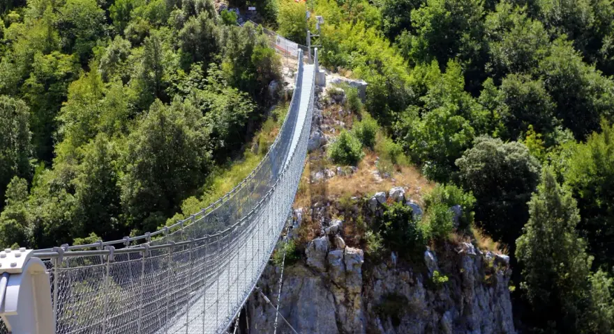 Un avventuroso percorso ponte tibetano si snoda tra rocce e fitta vegetazione, offrendo una vista mozzafiato sulla valle.