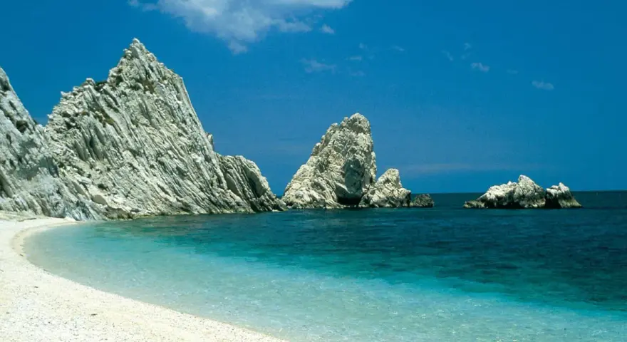 White pebble beach with turquoise water and dramatic white rock formations under a clear blue sky.