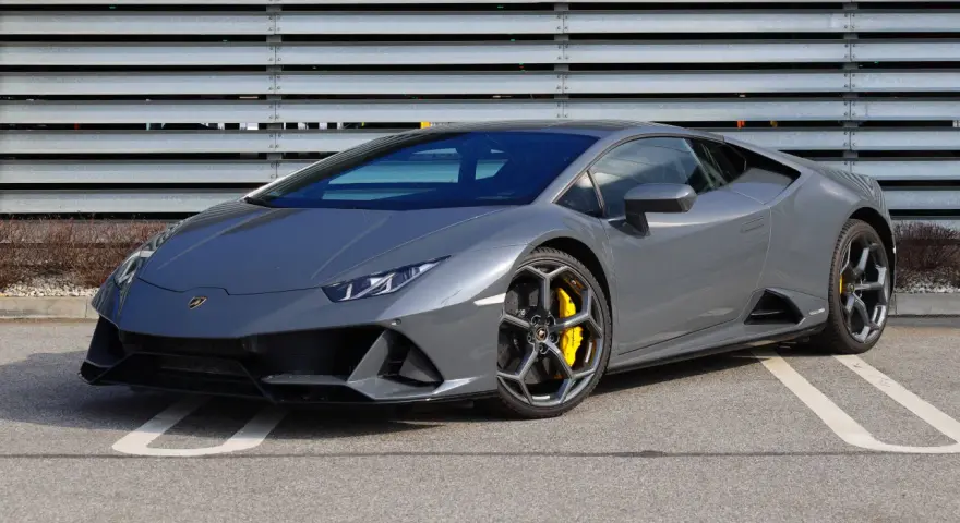 Szary Lamborghini Huracan z żółtymi zaciskami hamulcowymi na tle metalowej ściany.