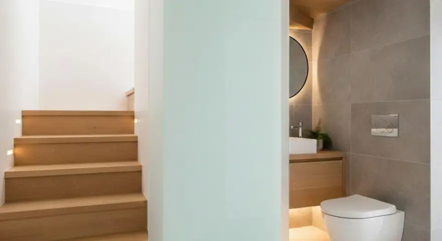 Escaliers en bois menant à un wc sous pente moderne, avec lavabo et miroir rond.