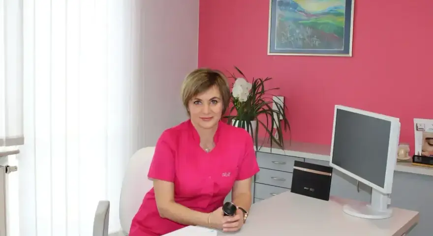 Lekarka w różowym uniformie siedzi przy biurku w gabinecie estetycznym.