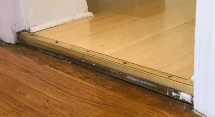 Próg z metalową listwą, widoczna różnica poziomów podłogi 4 cm między dwoma rodzajami drewna.