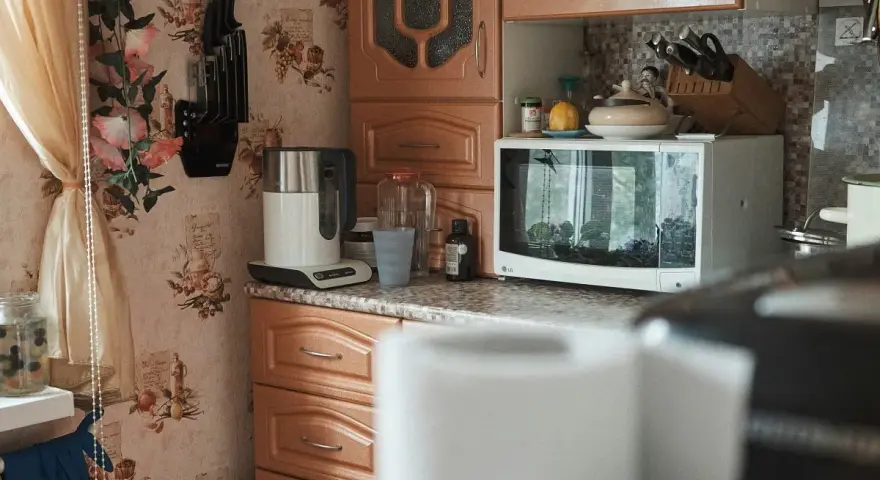 Kuchnia z kwiatową tapetą. Czy mikrofala może stać na lodówce? Tutaj stoi na blacie, obok czajnika i słoików.
